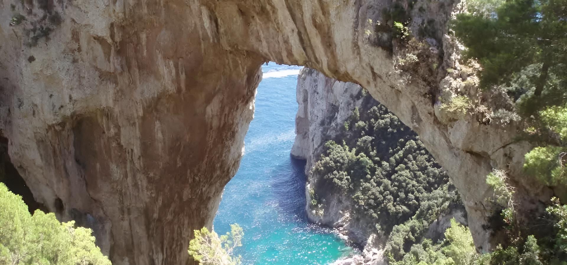 Arco naturale su mare turchese, circondato da scogliere e vegetazione rigogliosa.