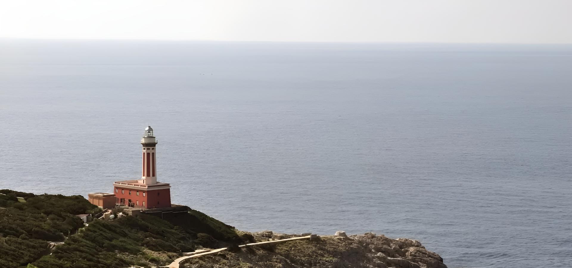 Faro solitario su scogliera verde, abbracciato dal mare infinito, sereno e maestoso.