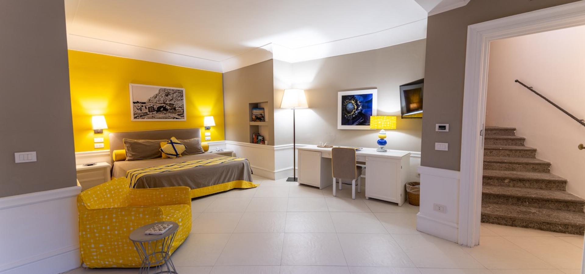 Camera luminosa, accogliente, con pareti gialle, letto elegante e scrivania moderna.