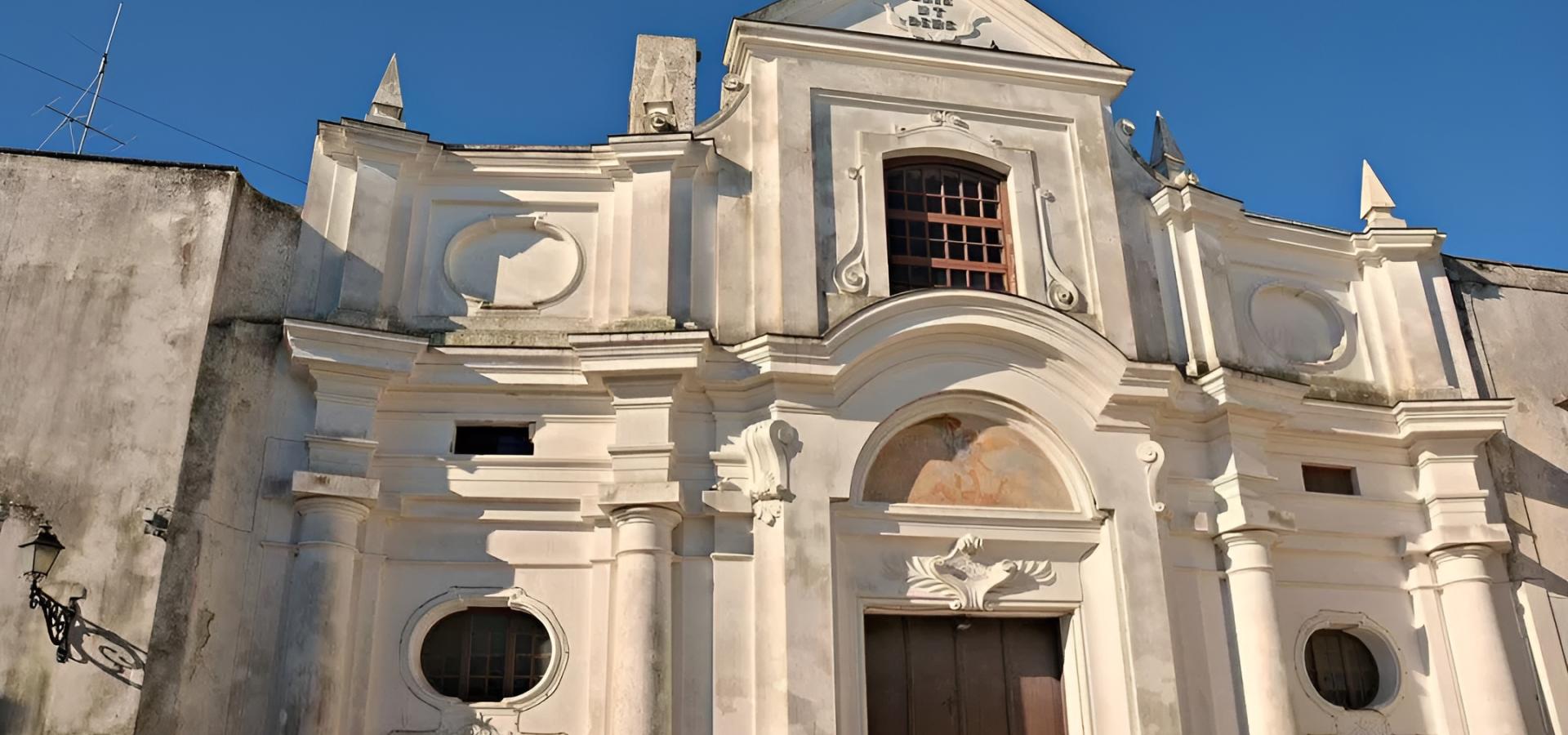 Facciata barocca di una chiesa, bianca e imponente, sotto un cielo azzurro intenso.