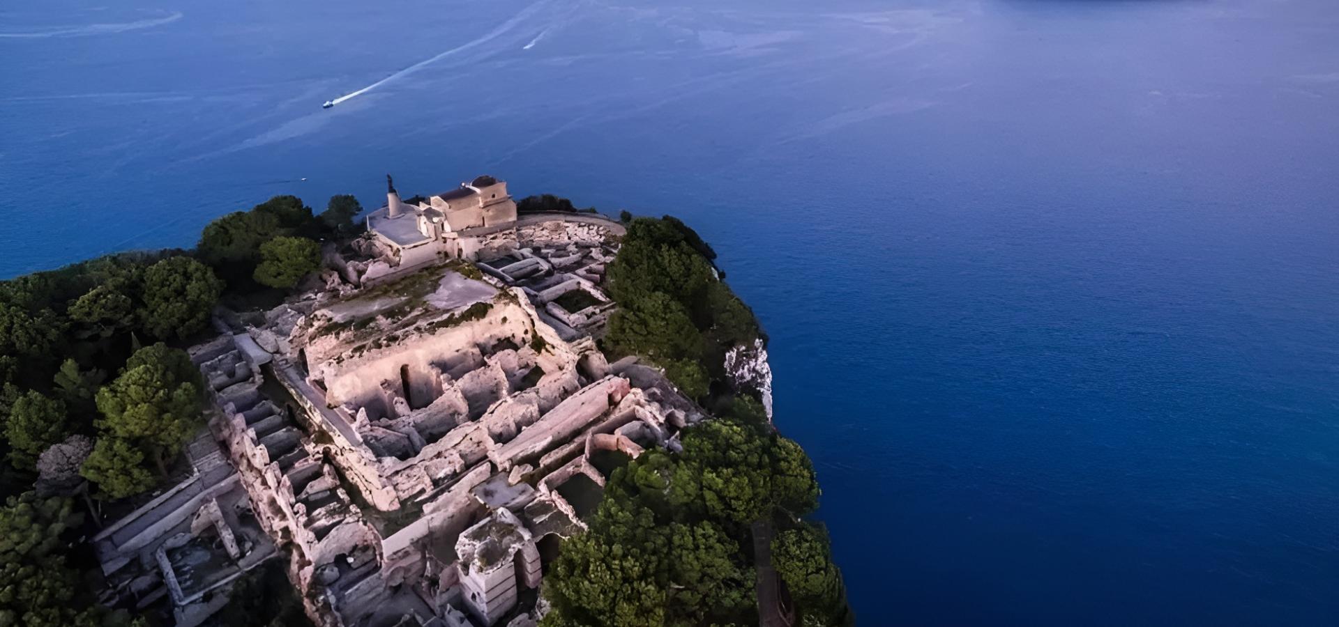 Vista aerea di rovine antiche su un'isola al tramonto, circondate dal mare blu.