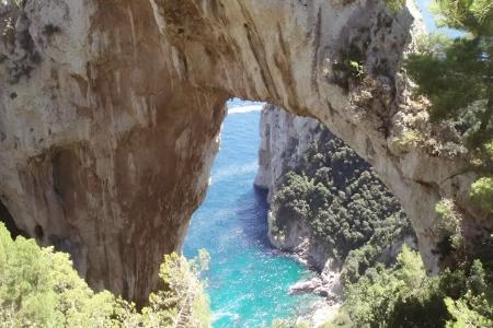 Arco naturale su mare turchese, circondato da scogliere e vegetazione rigogliosa.