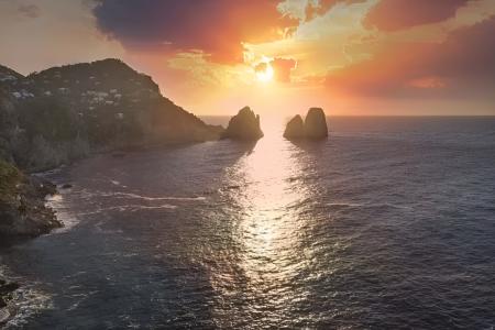 Tramonto mozzafiato sul mare, con faraglioni e cielo infuocato.