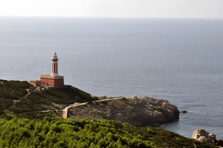 Faro solitario su scogliera verde, abbracciato dal mare infinito, sereno e maestoso.