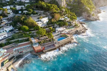 Vista aerea di una costa rocciosa con ville lussuose e mare azzurro scintillante.