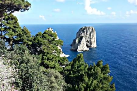 Scogliere imponenti emergono dal mare blu, circondate da verdi pini rigogliosi.