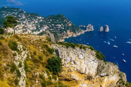 Vista mozzafiato di Capri, rocce imponenti e mare blu intenso, barche sparse.