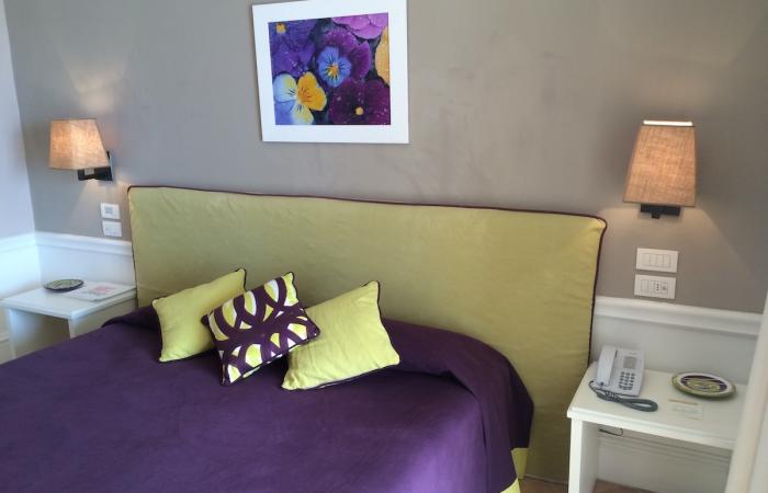 Camera accogliente con letto viola e verde, lampade soffuse, arte floreale vibrante.