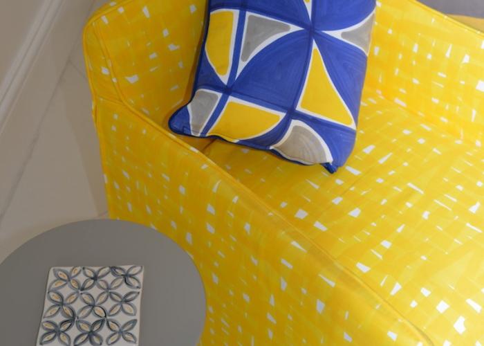 Divano giallo vivace con cuscino geometrico blu e giallo, tavolino grigio elegante.