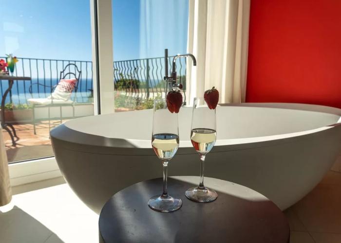 Vasca con vista mare, calici di vino e fragole, atmosfera di relax e lusso.