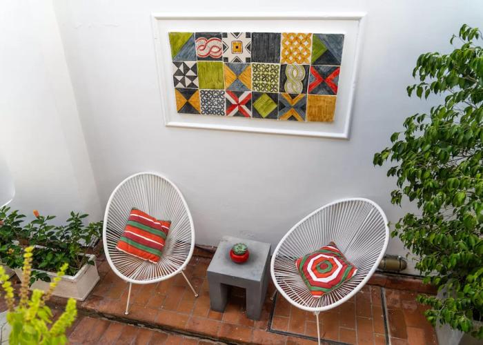 Due sedie bianche, cuscini colorati, arte geometrica, piante verdi: un angolo accogliente e vivace.