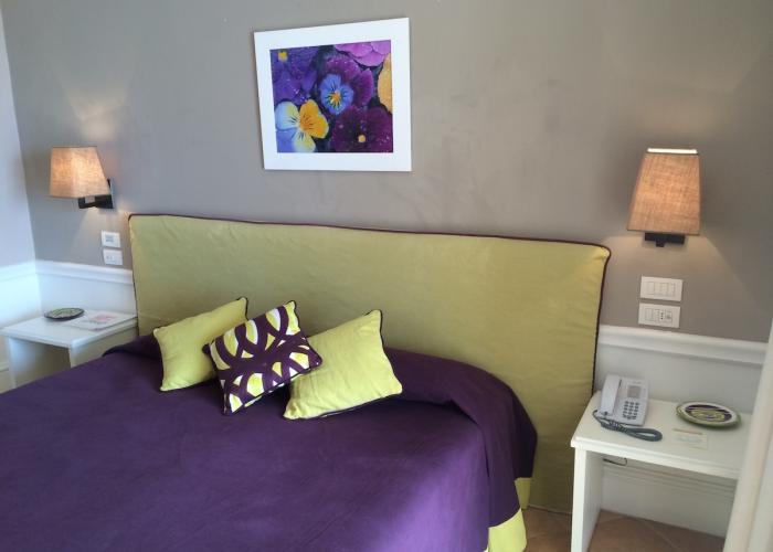 Camera accogliente con letto viola e verde, lampade soffuse, arte floreale vibrante.