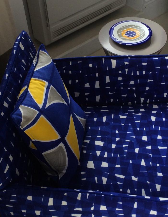 Divano blu con cuscino colorato, piatto decorativo su tavolino.